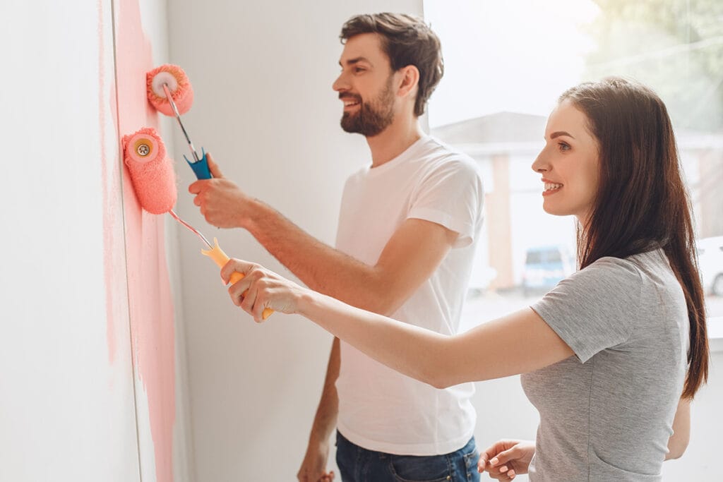 Man and woman using rollers to paint a wall pink