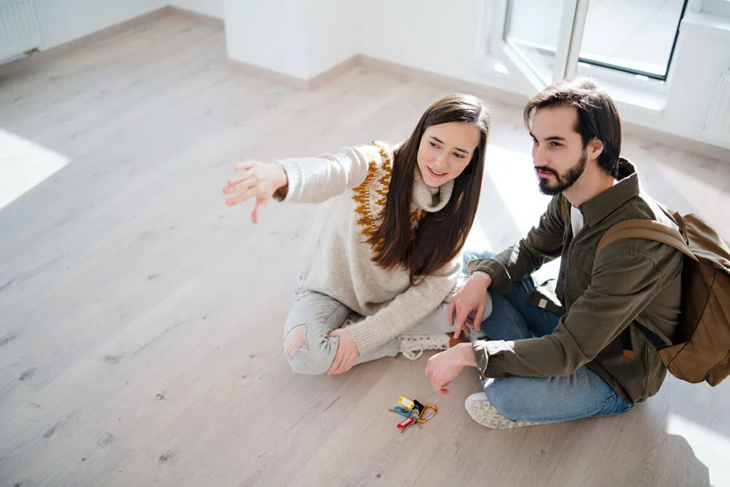 Couple sat on floor of new property, pointing towards the distance